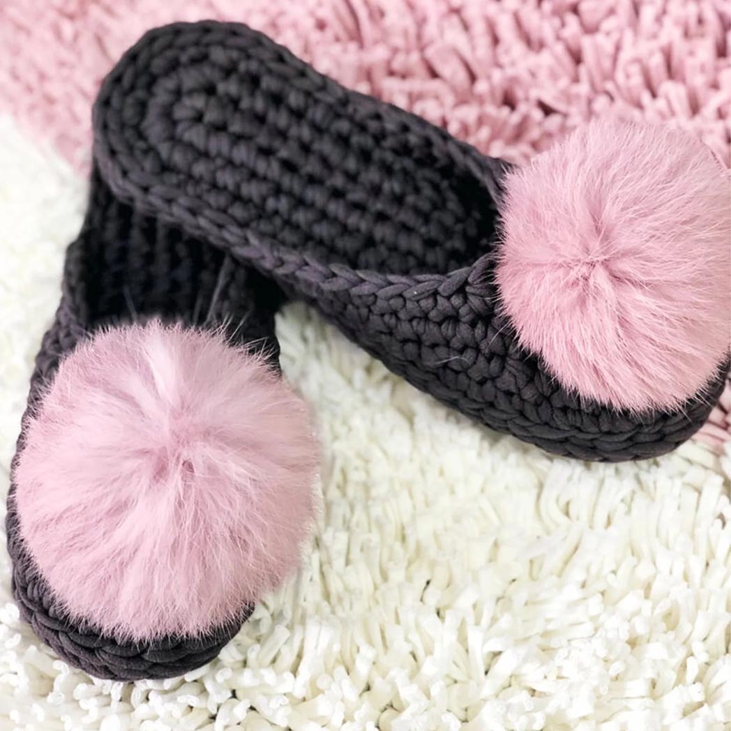 Two black crocheted slippers with pink pom poms.