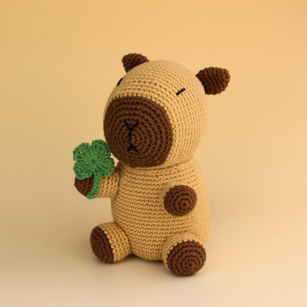 Hardicraft DIY Crochet Kit - Cato Capibara on a gradient orange background with a green four leaf clover.