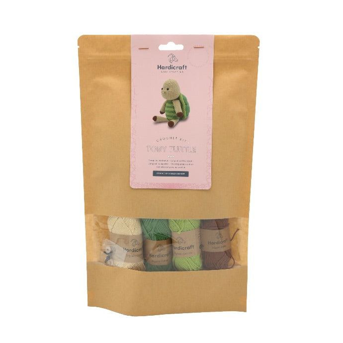 Hardicraft DIY Crochet Kit - Toby Turtle Brown packaging with a pink vertical label and a window showing 4 balls of yarn in colors cream, brown, light green and dark green.
