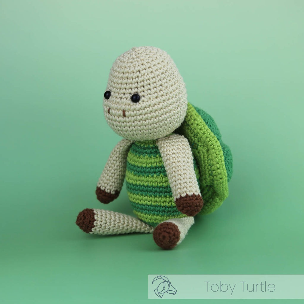 Hardicraft DIY Crochet Kit - Toby Turtle tan turtle with a striped green shell on a gradient green background.
