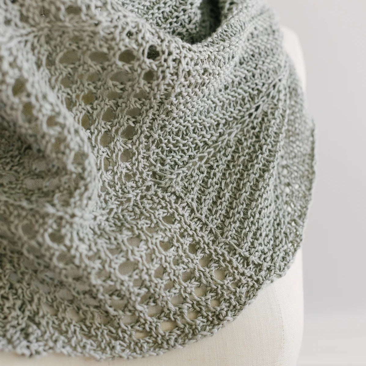 Close-up of a sage green Villa cowl by Quince & Co. on a dress form, showing garter ridges and a mesh eyelet border