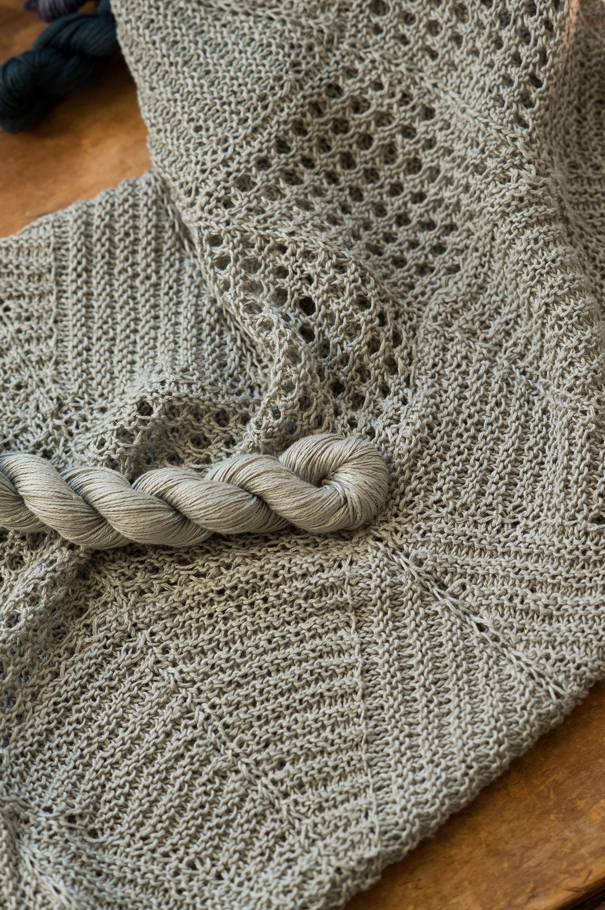 Sage green Villa cowl by Quince & Co. laid flat with a matching skein of Sparrow yarn, showing eyelet and garter sections