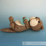 Hardicraft DIY Crochet Kit - Ole Otter with a teal fish held between the otters hands lying on it's back in front of a gradient blue background.