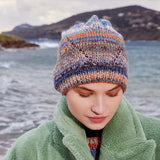 Woman wearing the Clio Hat by Lang Yarns, a marled beanie striped in blue, orange, gray, and navy with an eyelet zigzag