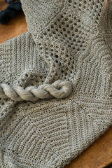 Sage green Villa cowl by Quince & Co. laid flat with a matching skein of Sparrow yarn, showing eyelet and garter sections