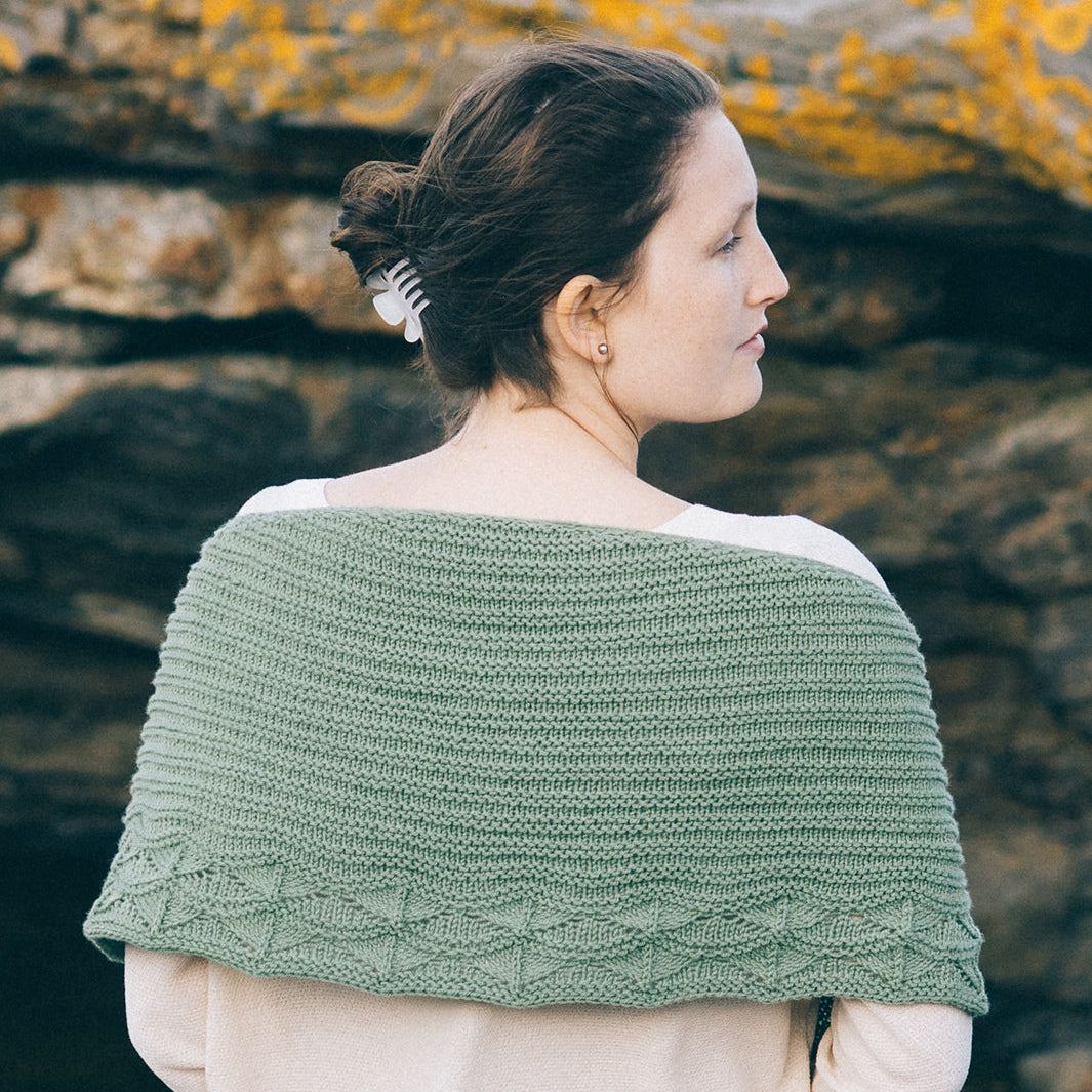 Back view of the Cave Point shawl draped over a woman’s shoulders, garter body and lace border in green Quince & Co. Chickadee